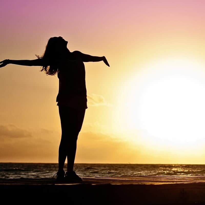 Sunset silhouette of a woman with outstretched arms on the beach.
