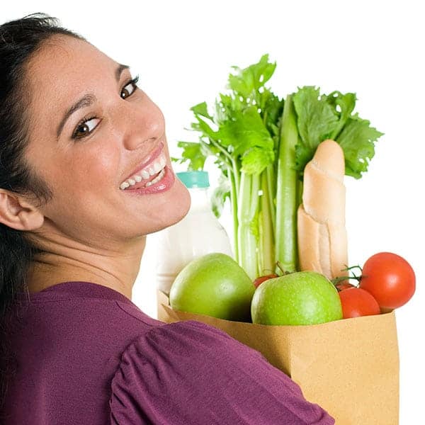Fresh green vegetables and apples in a paper bag with a smiling woman.