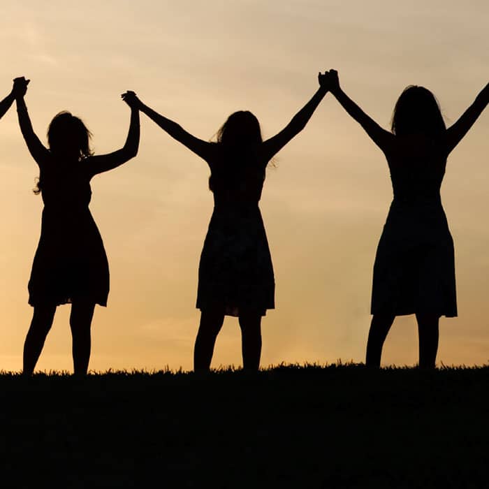 Sunset silhouettes of three women holding hands