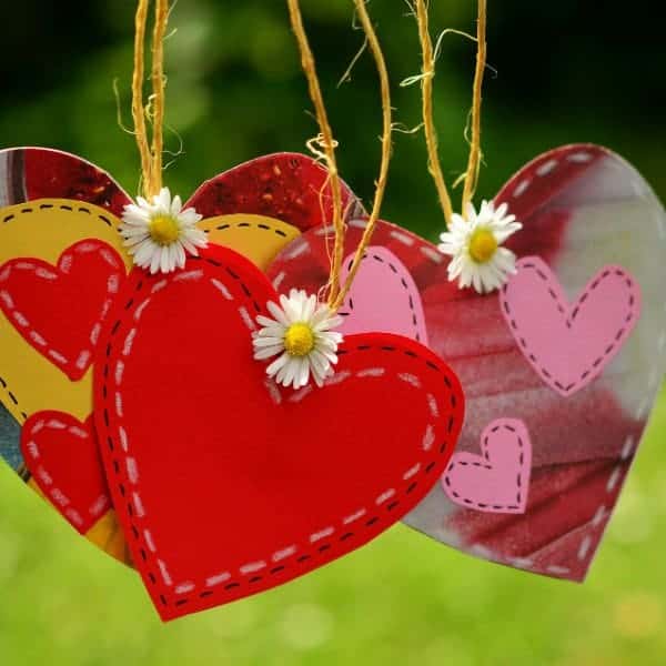 Colorful hanging heart decorations with daisies, outdoor background, symbolizing love and celebration.
