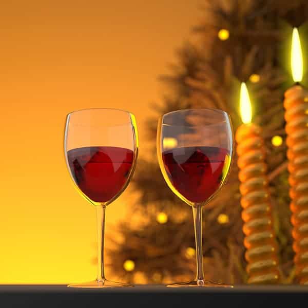 Red wine glasses on a table with Christmas candles and tree in the background.