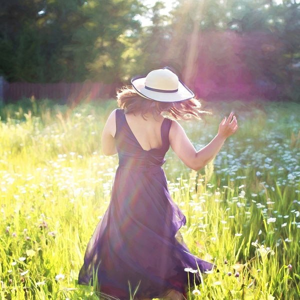 Serene woman in a flowing dress enjoying sunlight in a lush field
