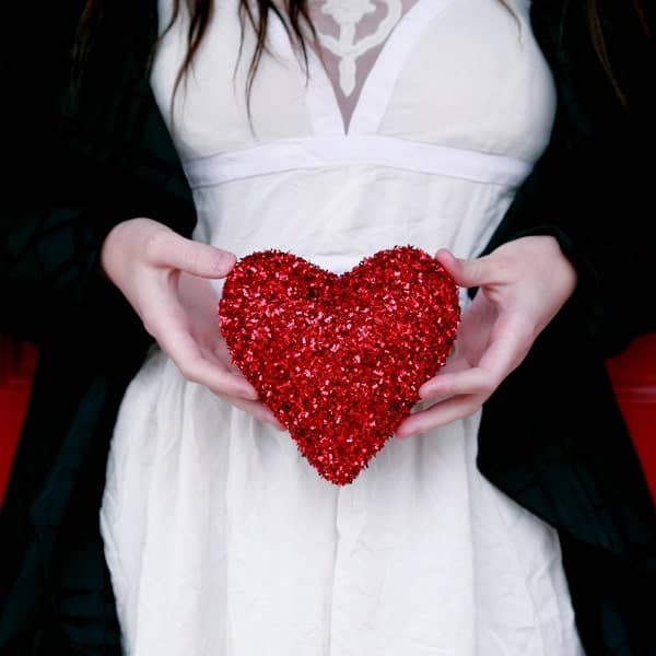 Shaped red glitter ornament held by a woman in a white dress and black jacket.