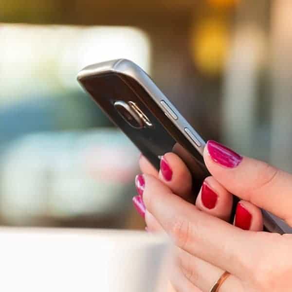Smartphone with pink nail polish held by a person.