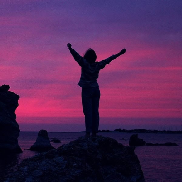Sunset silhouette of a person on rocks by the ocean