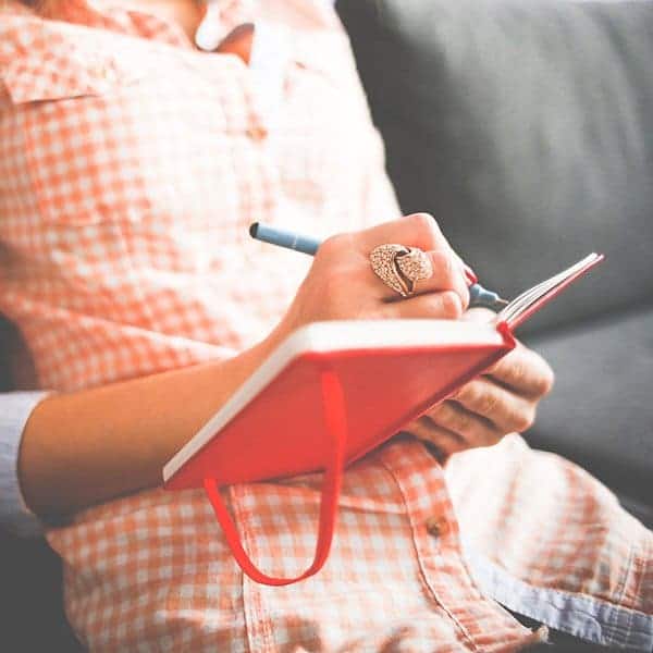 Creative journal writing in a cozy setting with a person holding a red notebook and pen.