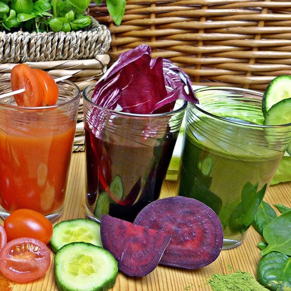 Fresh vegetable juices with colorful beets, cucumbers, and tomatoes in glass cups for healthy living and nutrition.