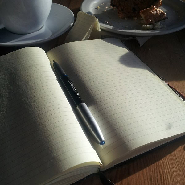 Notebook with a pen on an open page, sunlight illuminating the scene.