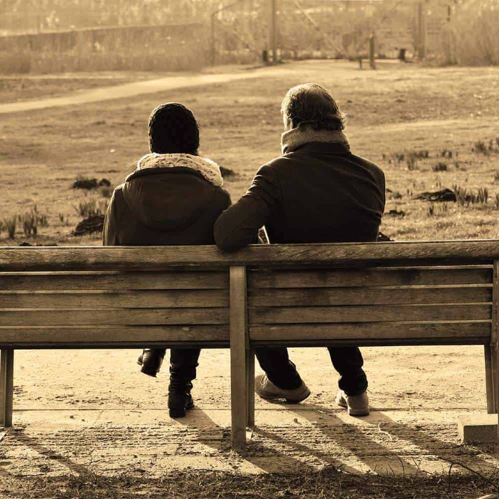 Aging couple sitting on park bench, enjoying peaceful moment together.