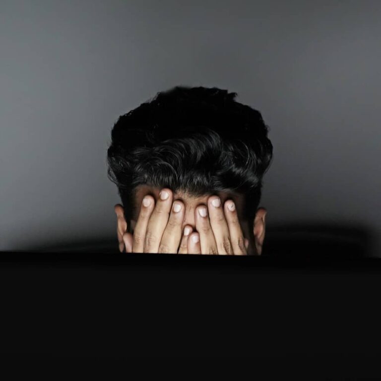 Young man covering face with hands in a dark setting