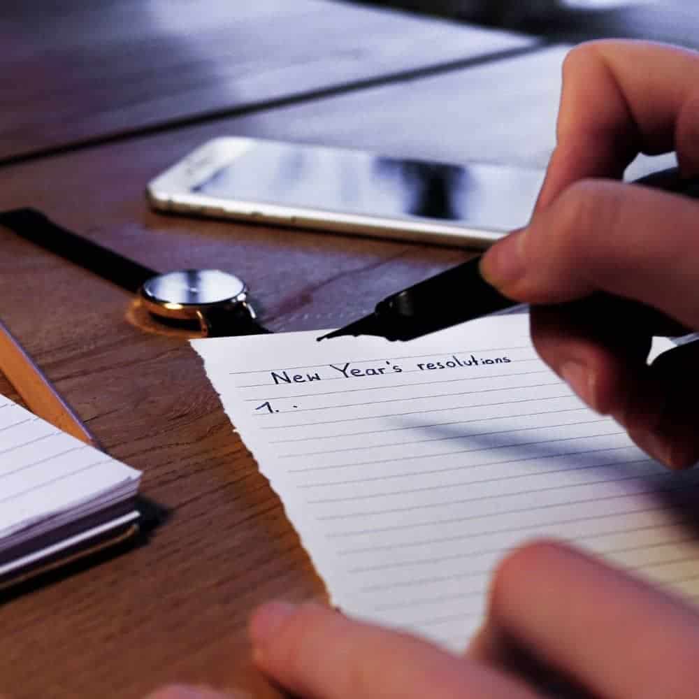 Handwriting New Year's resolutions on lined paper with a pen on a wooden desk.