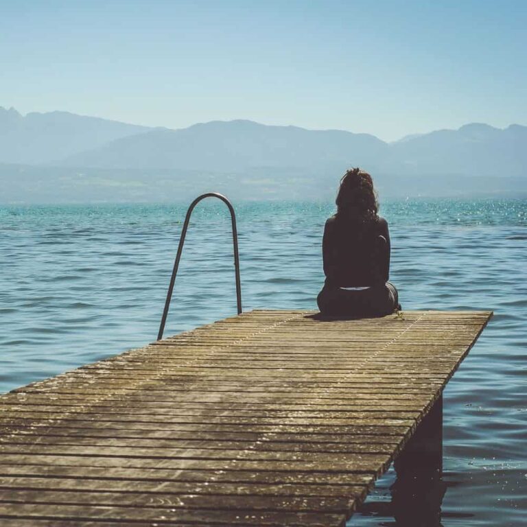 Peaceful woman sitting on dock by lake, embracing connection and wellbeing.