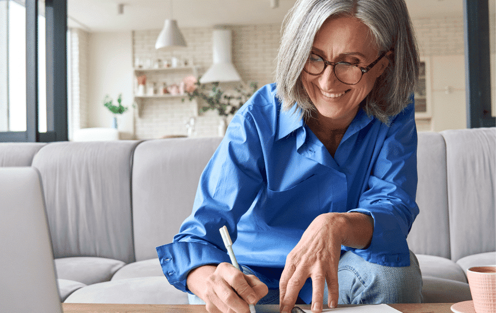 Elderly woman writing in a notebook at home, engaging in creative writing.